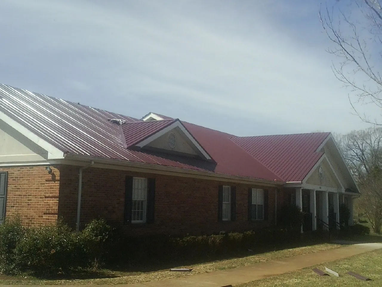 Red metal roof with gabled entries on a long brick building, from a Hail Damage Roof Repair job in South Sutton