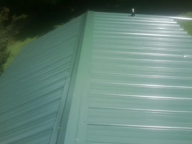 New green metal panels meeting at the ridge of a roof — Flat Roof Repair work by our crew in South Sutton