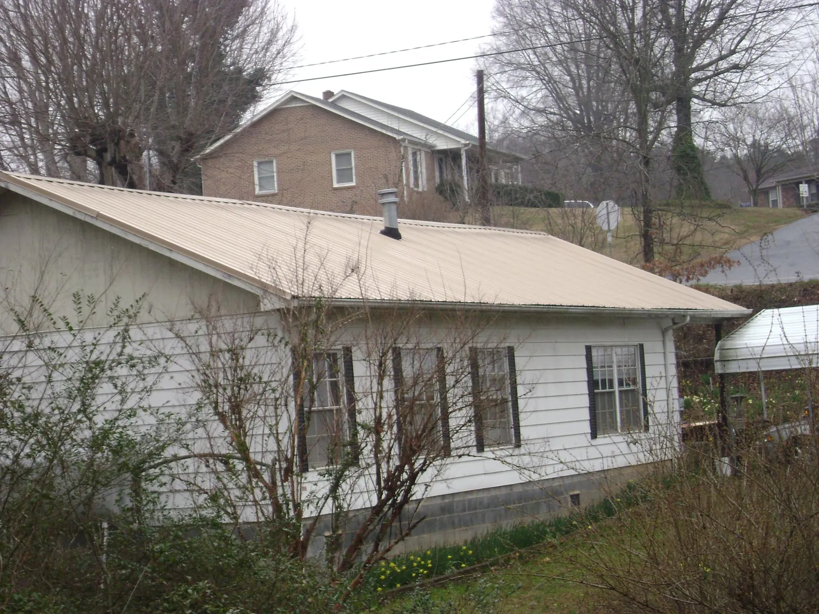 Tan metal roof on a white sided house set into a hillside — Commercial Roofing by Roofing Brothers in South Sutton