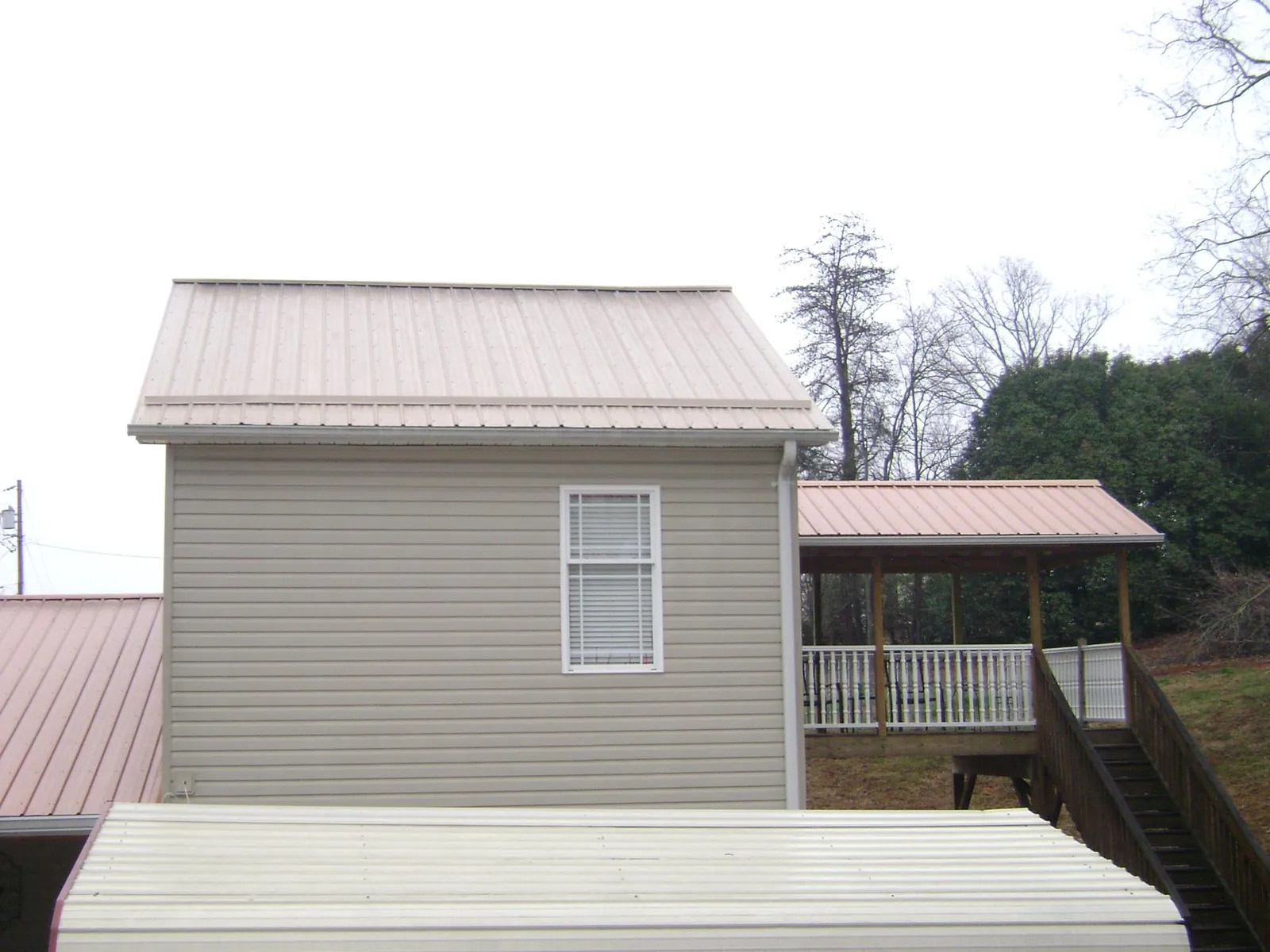 Tan metal roofs on a two story addition and attached porch, from a Roof Replacement job in South Sutton